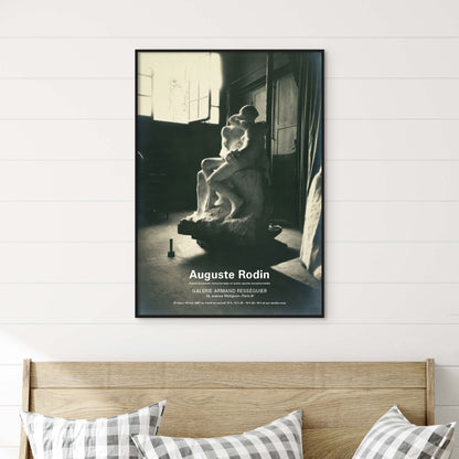 A framed black and white art print of Auguste Rodin's sculpture 'Galérien Armado' displayed on a white shiplap wall above a wooden headboard with gingham pillows.