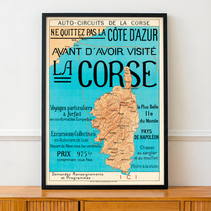 Framed map poster of Corsica with promotional text on a wall.