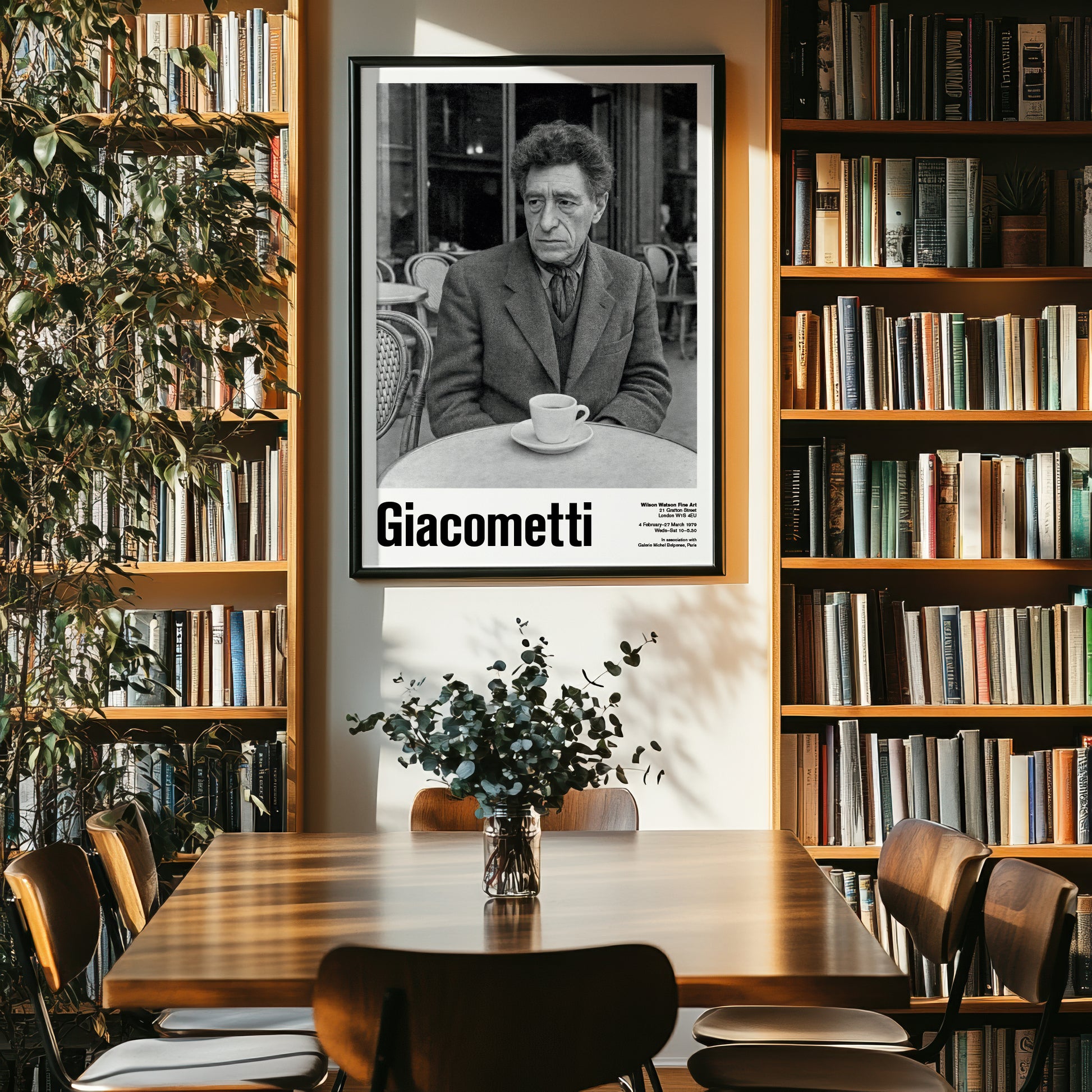Library or study room with bookshelves, a table, chairs, and a framed picture of a man named Giacometti.