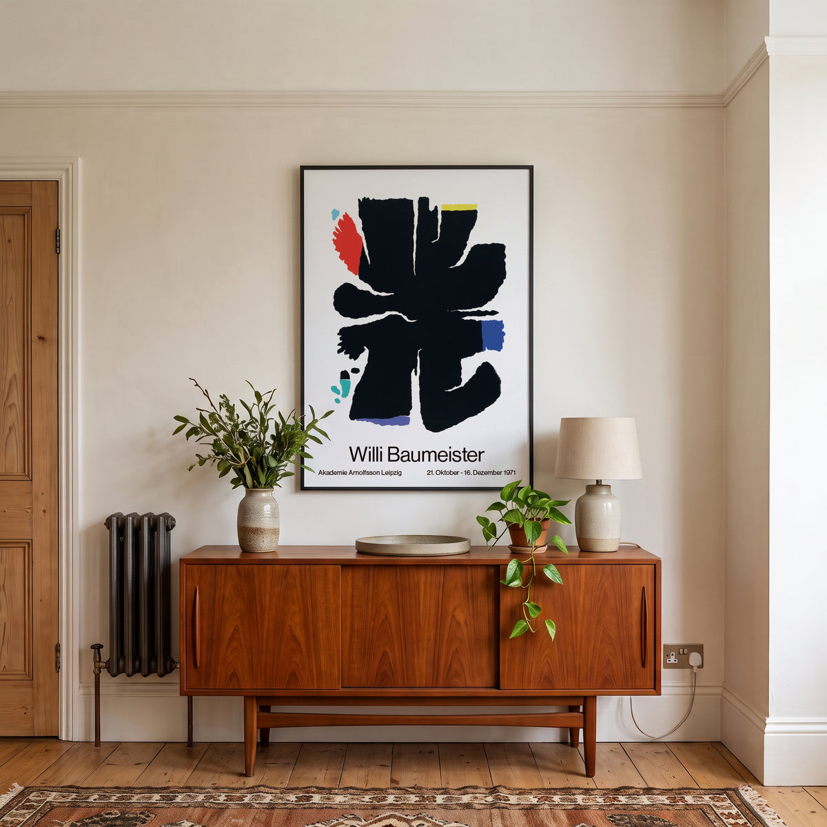 A framed art print of Willi Baumeister's abstract black brushstroke design hangs on a cream-colored wall above a mid-century modern wooden credenza in a styled room setting.